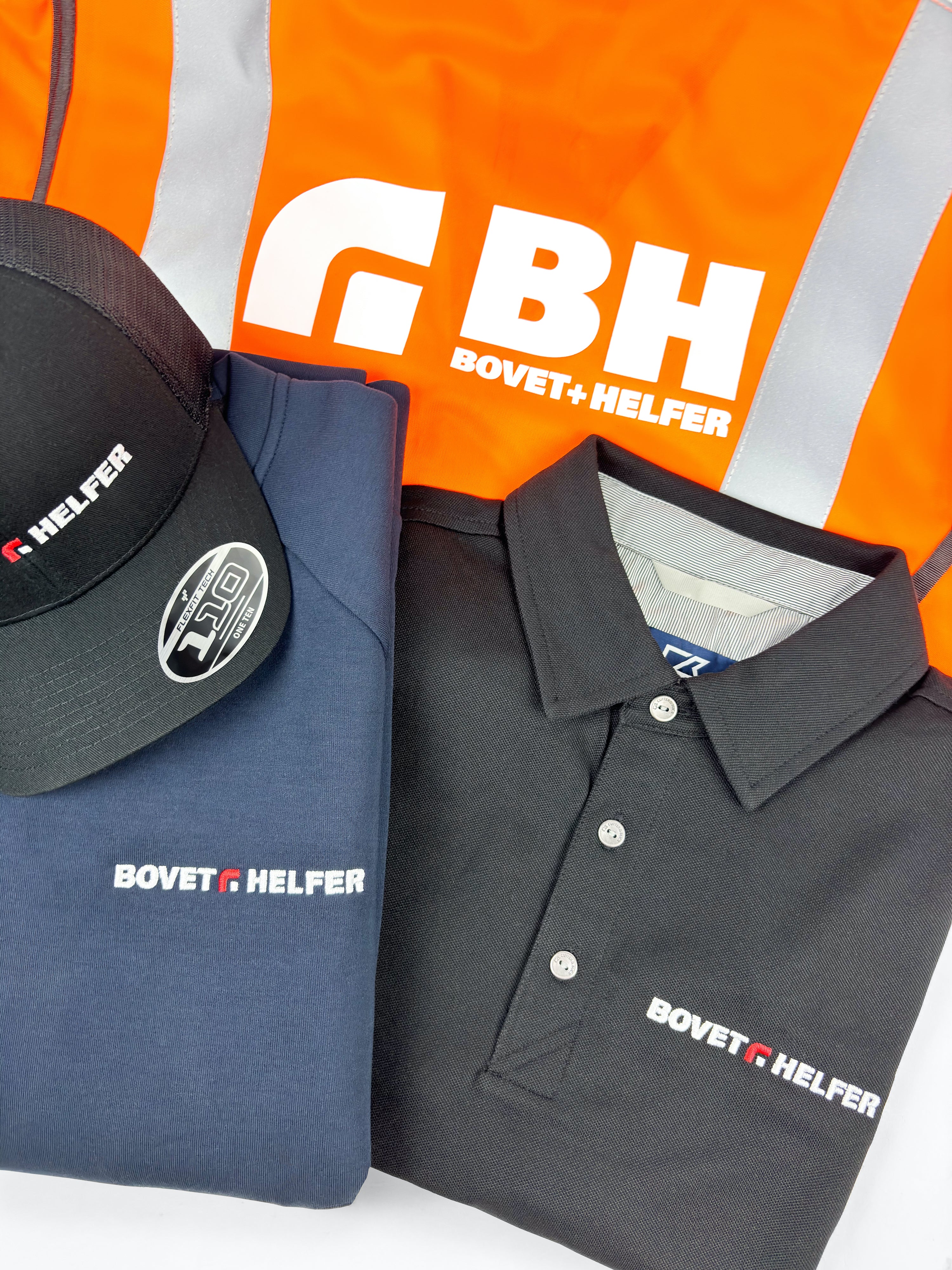 Casquette, sweat bleu marine et polo noir brodés Bovet+Helfer, posés sur un gilet orange réfléchissant.